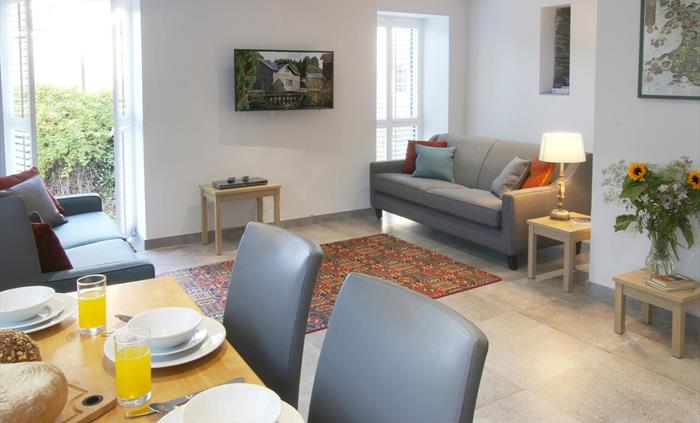 Spacious and bright open-plan lounge and dining area with two sofas, a flat-screen TV, and a set table.